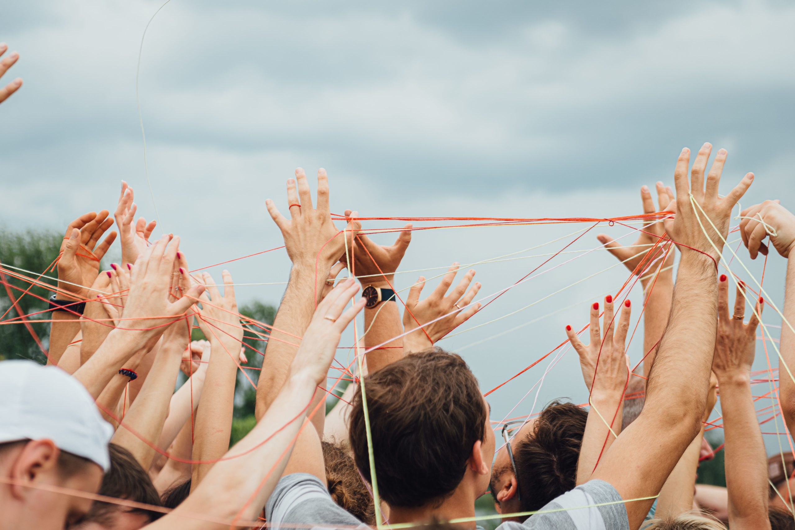 Hands of people, connected by a thread, during an open air corporate team building