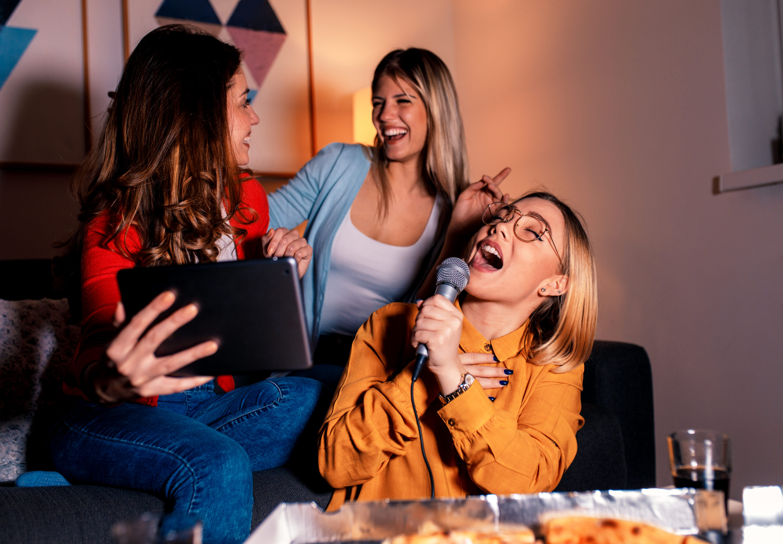 Three female friends having fun playing karaoke at home.