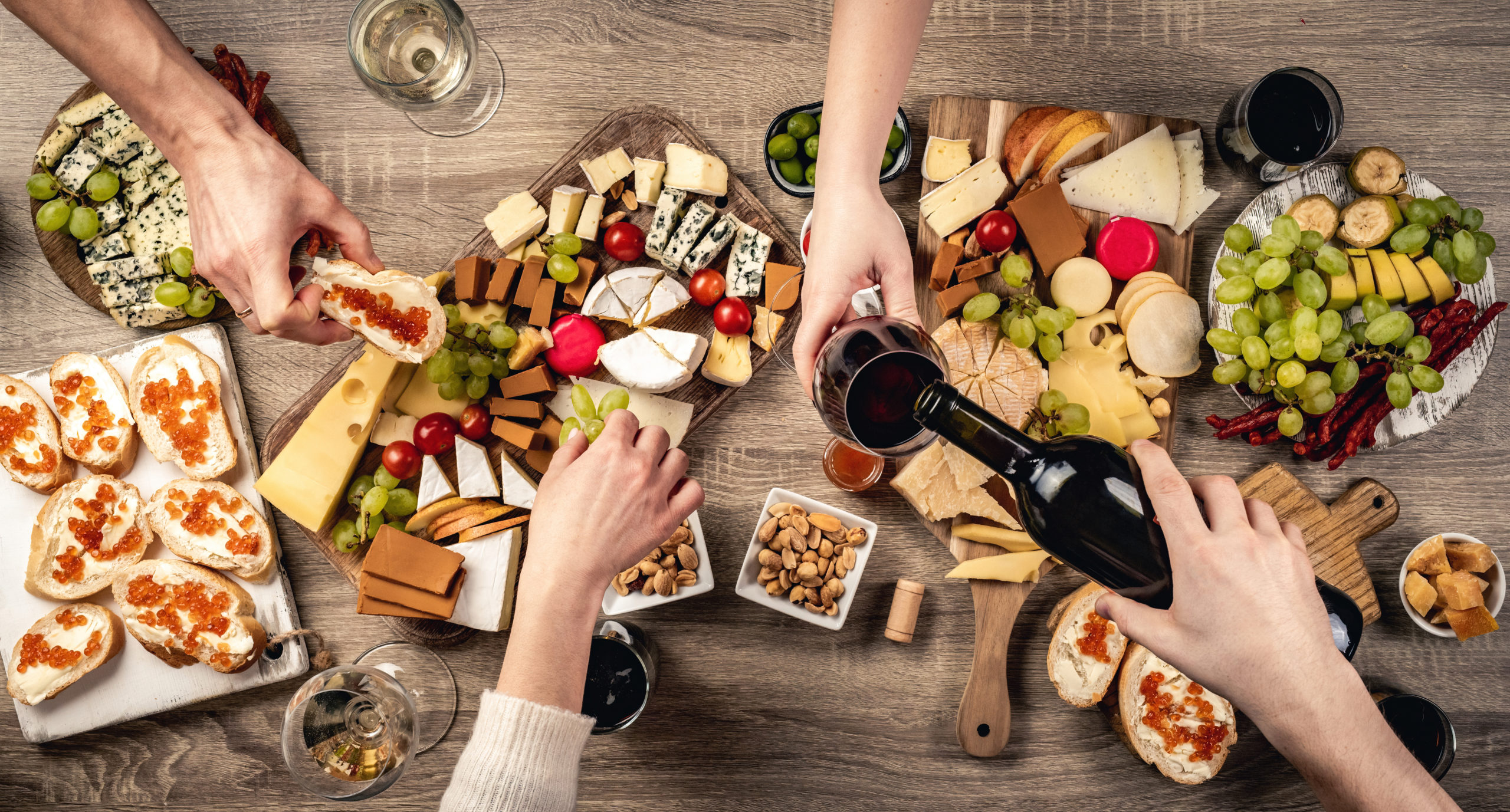 People hands with wine glasses, grape and variety of cheese kinnds. Delicatessen food collection with alcohol beverage